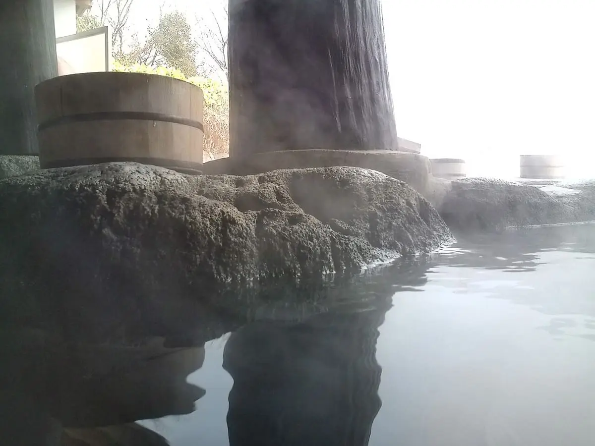 Steam over a rock edged outdoor hot spring bath with wooden buckets at Musoen in Yufuin