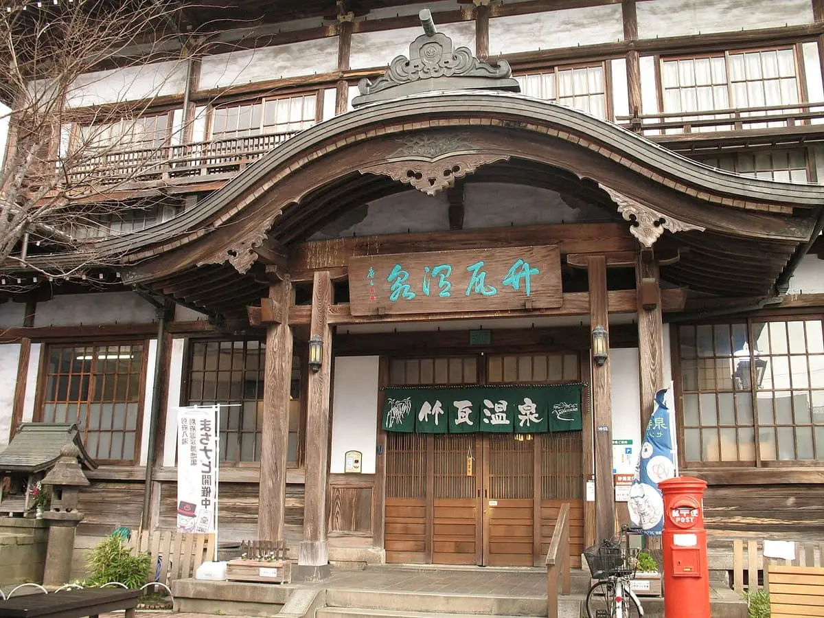 Ornate curved gable entrance of Takegawara Onsen with its wooden name board