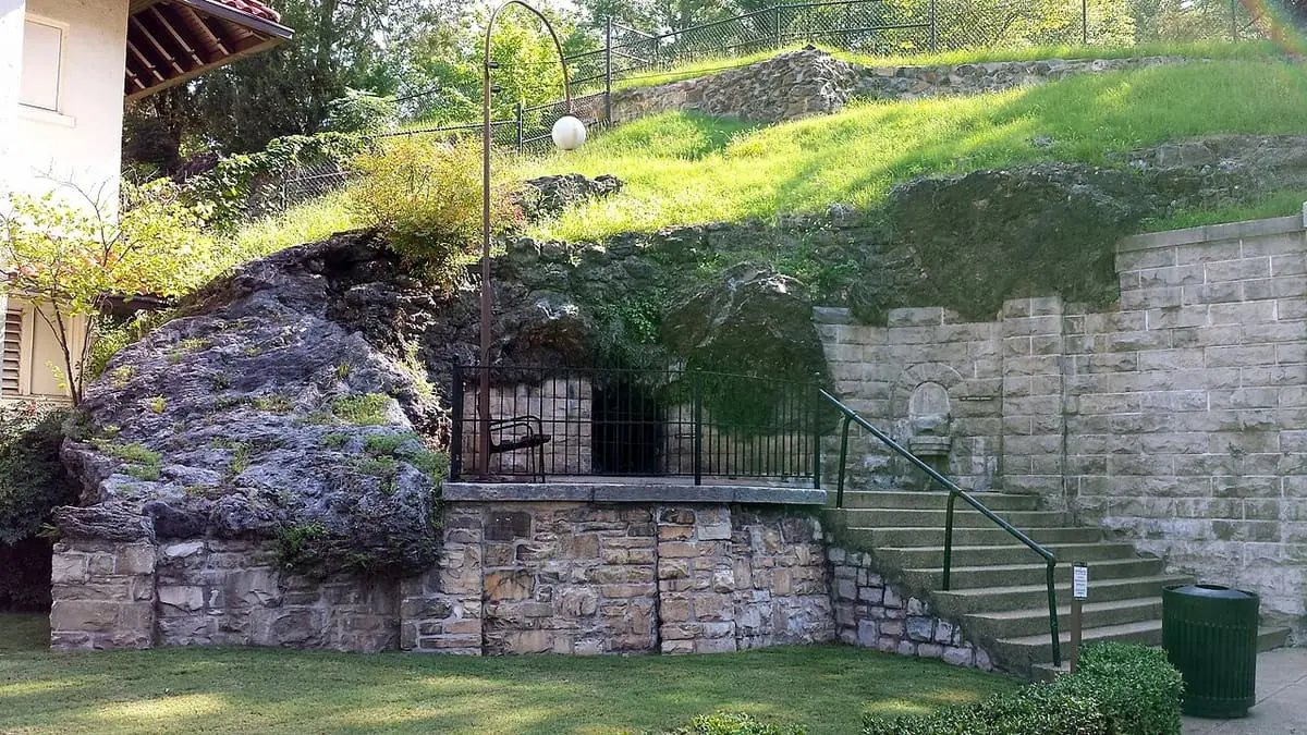 Tufa rock outcrop, stone retaining wall and arched spring niche beside steps on a grassy slope