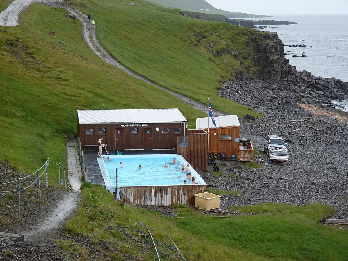 Krossneslaug pool and hut below a green hillside at the edge of the sea in Strandir