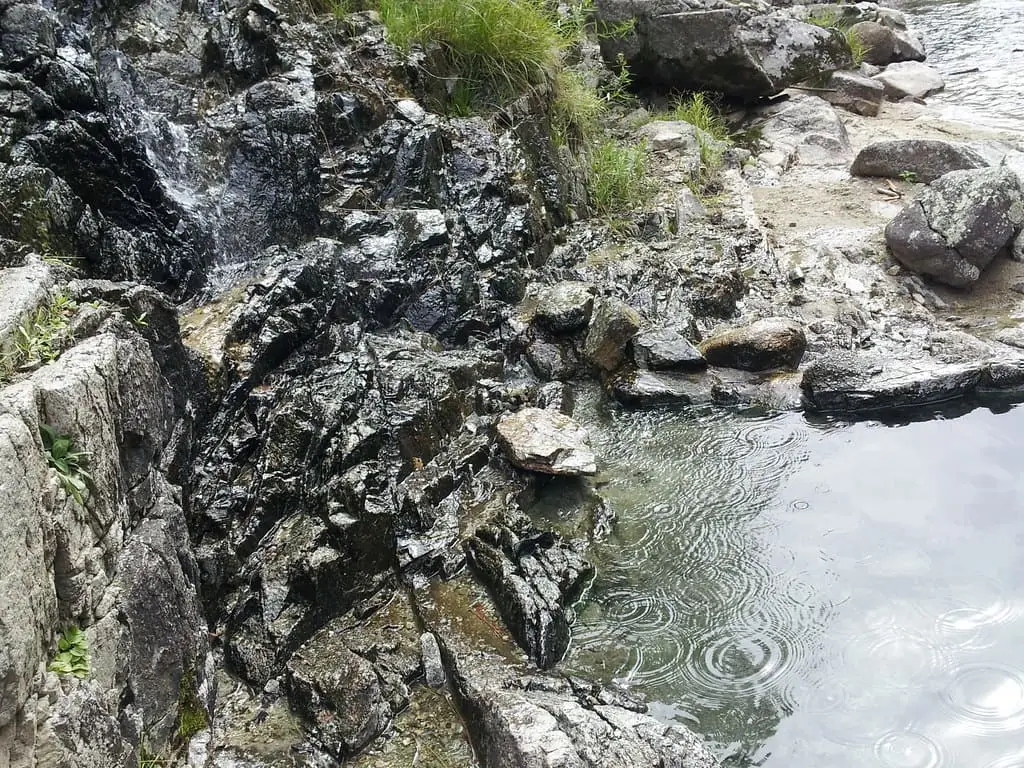 Hot water running over dark wet rocks into a calm pool at Mile 16 Hot Springs
