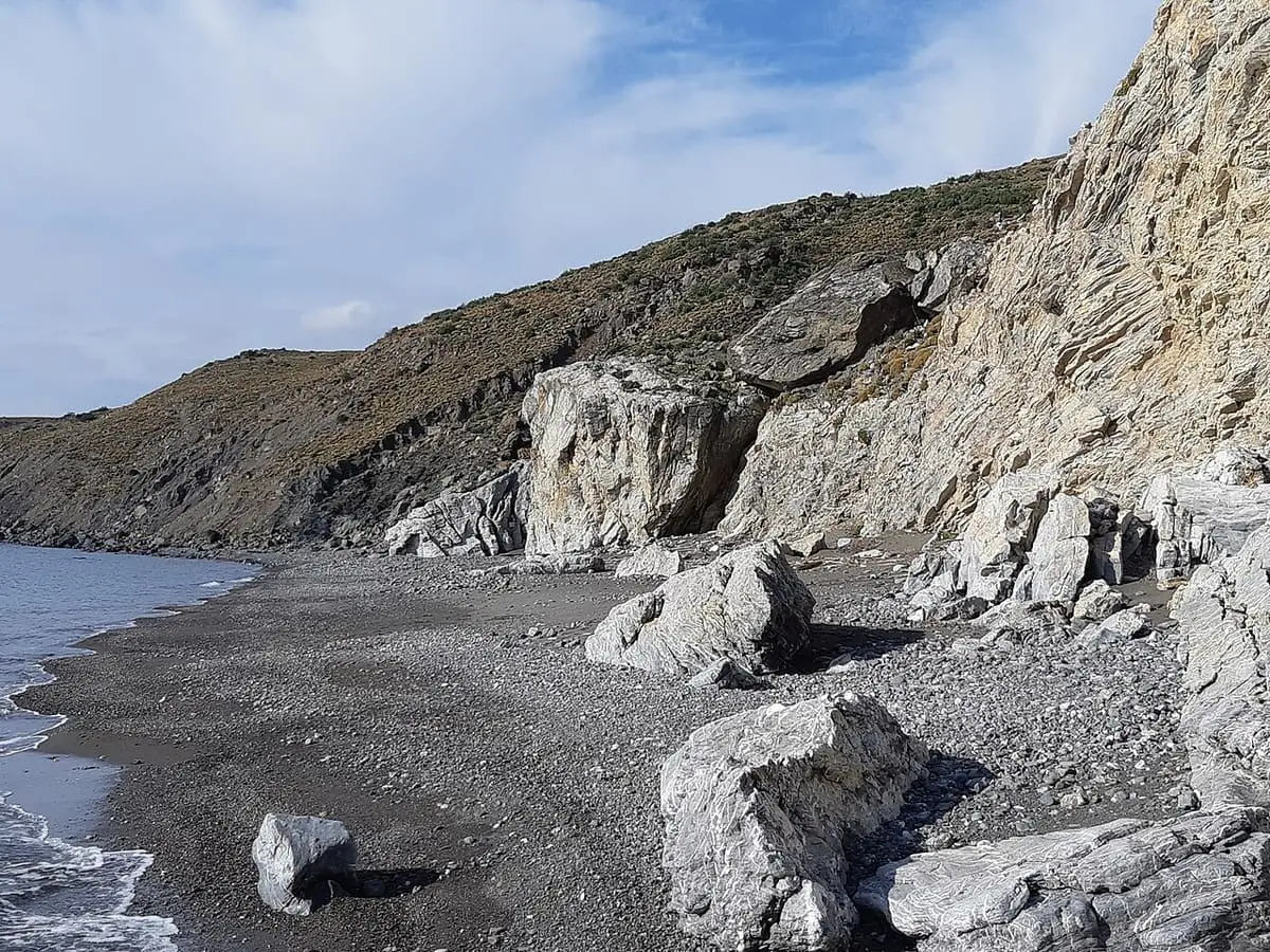 Dark pebble beach and pale boulders beneath the cliffs at Embros Thermae on Kos