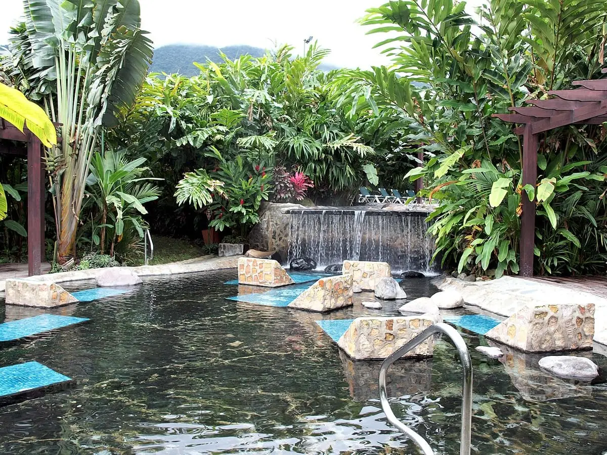 Rock edged hot spring pool with a small waterfall and lush gardens at Baldi