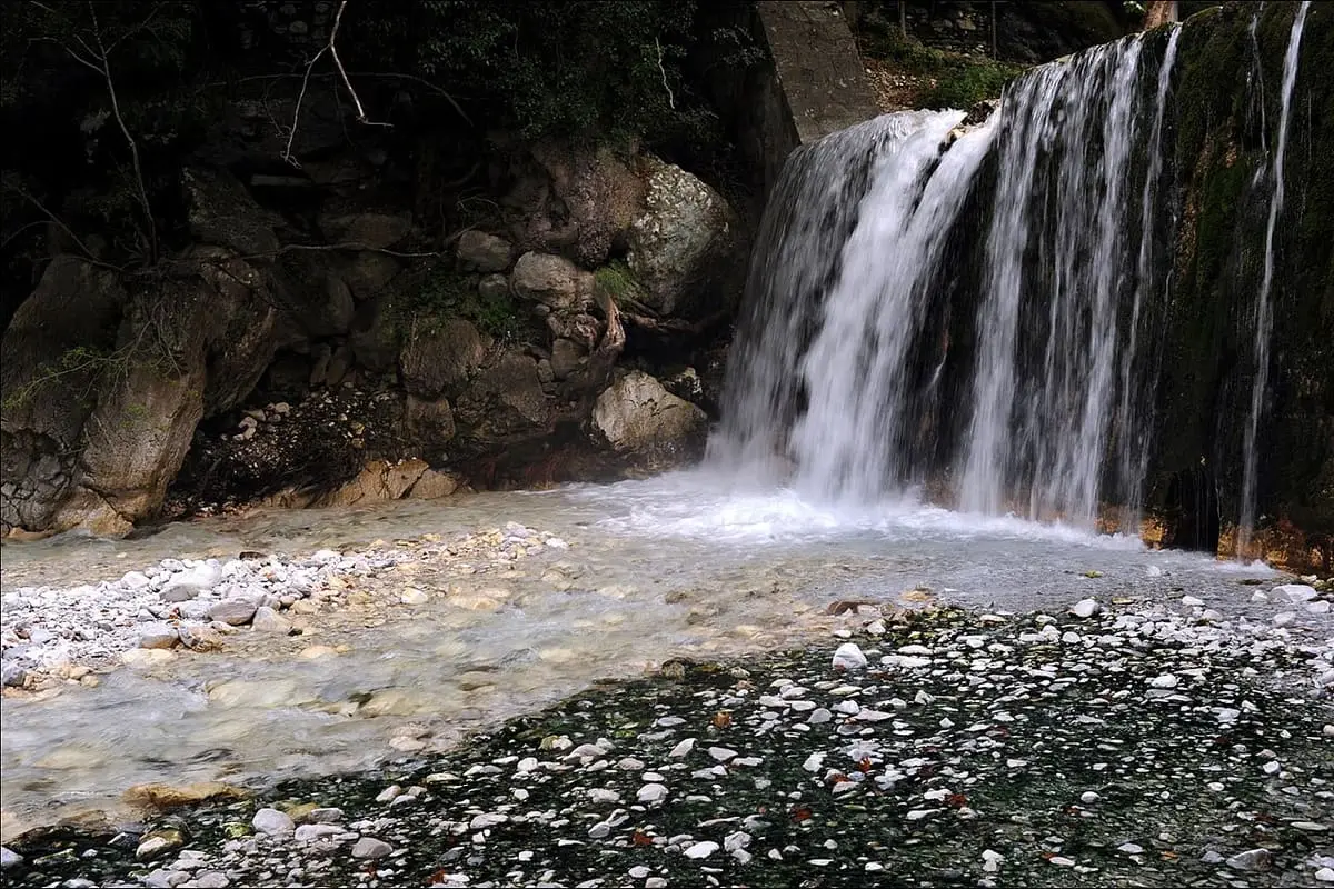Warm waterfall pouring onto a pebbly riverbed in the Loutra Pozar gorge