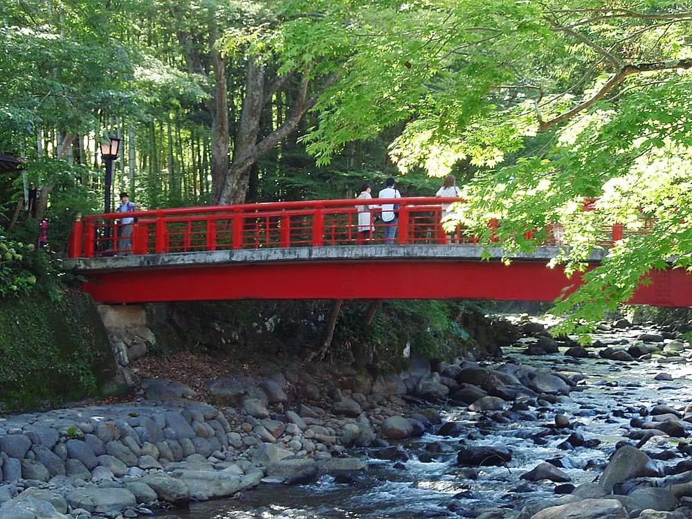 Red Katsura bridge over the rocky Shuzenji River under fresh green maple trees