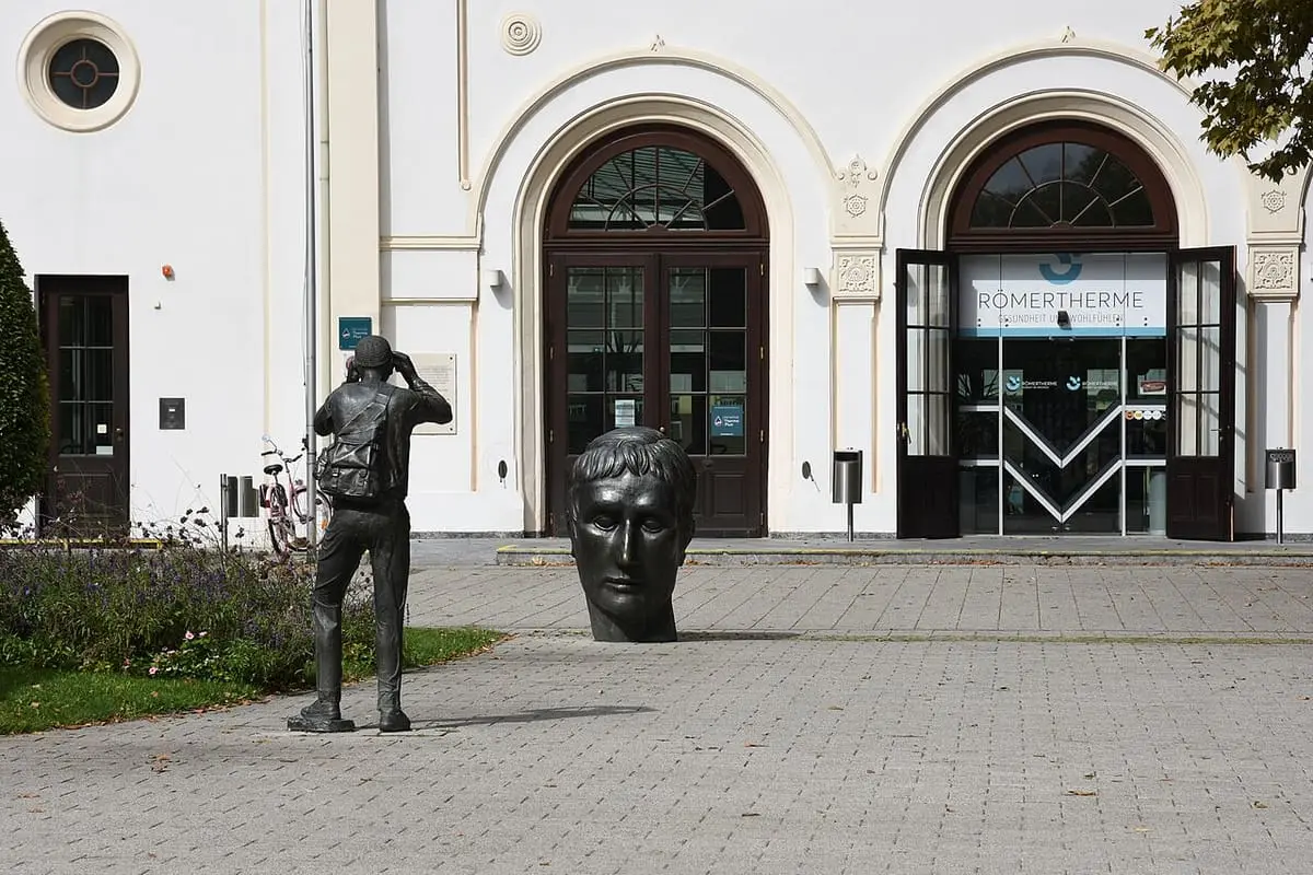 Arched entrance of the Römertherme Baden with bronze sculptures standing on the forecourt