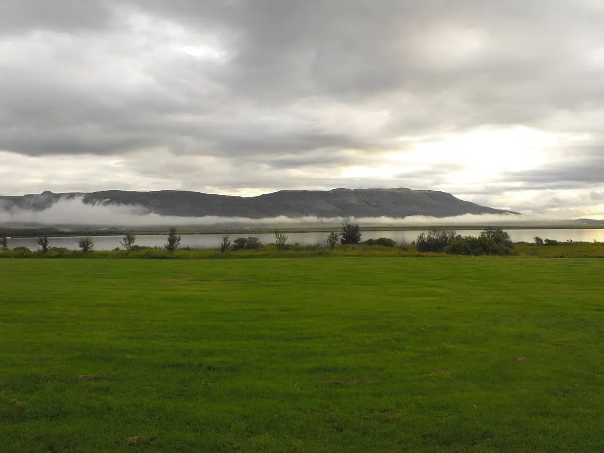 Low cloud over the mountains across Lake Laugarvatn seen from a green shore meadow