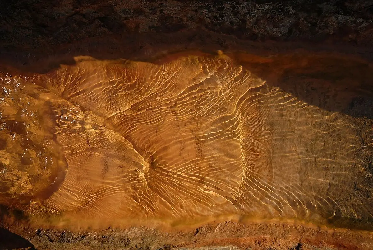 Close view of orange mineral deposits rippling under the hot spring water at Loutra, Kythnos
