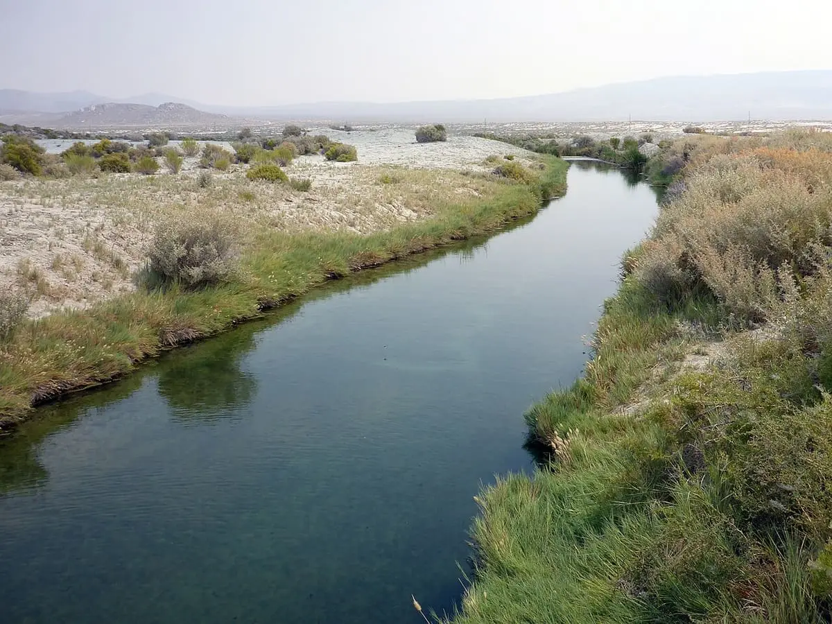 Long straight hot spring ditch at Trego lined with reeds and sagebrush under hazy mountains