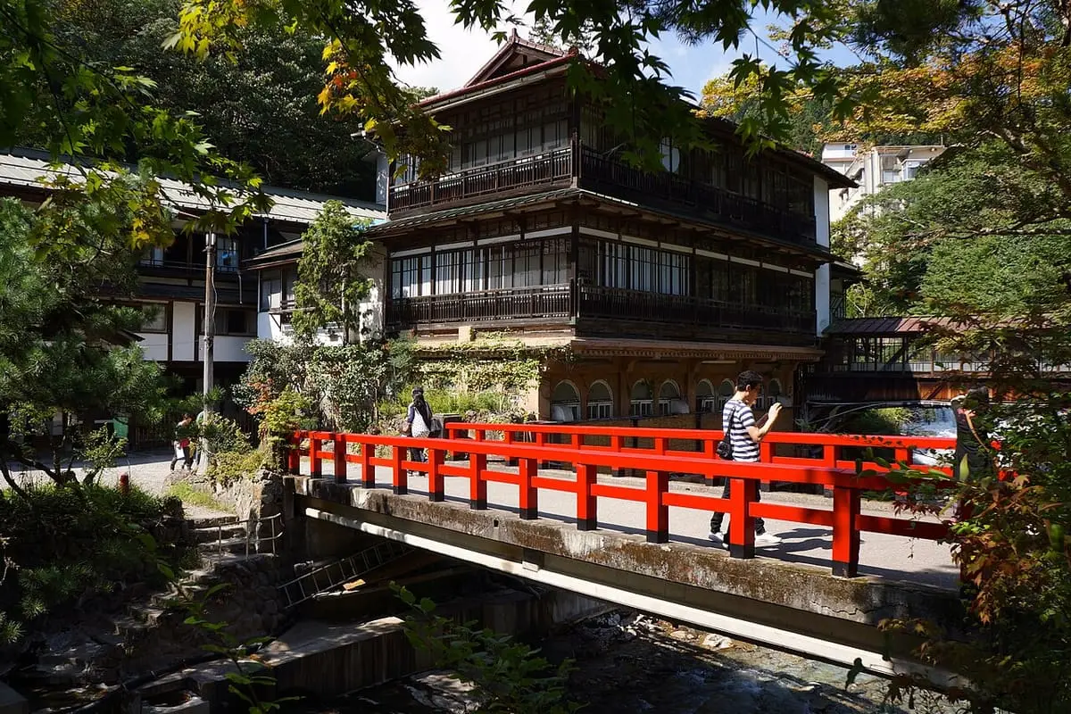 Historic wooden Sekizenkan inn with a red bridge over a stream at Shima Onsen