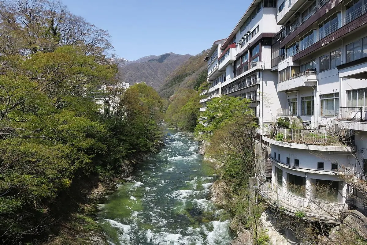 Rushing river below the tall Minakamikan inn among spring greenery at Minakami Onsen