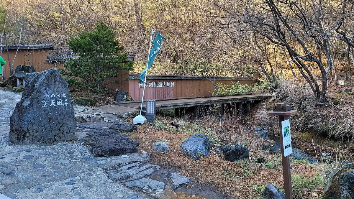Stone marker and wooden fence at the entrance to Sainokawara Rotenburo