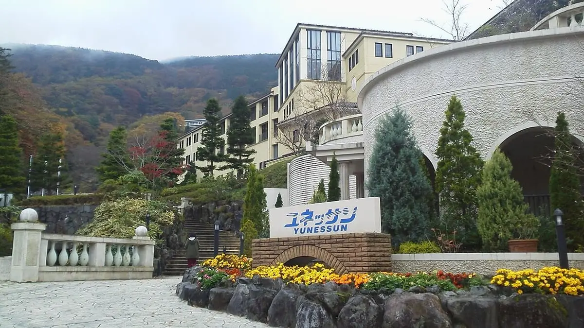 Yunessun entrance sign with flower beds in front of the curved resort building in Hakone