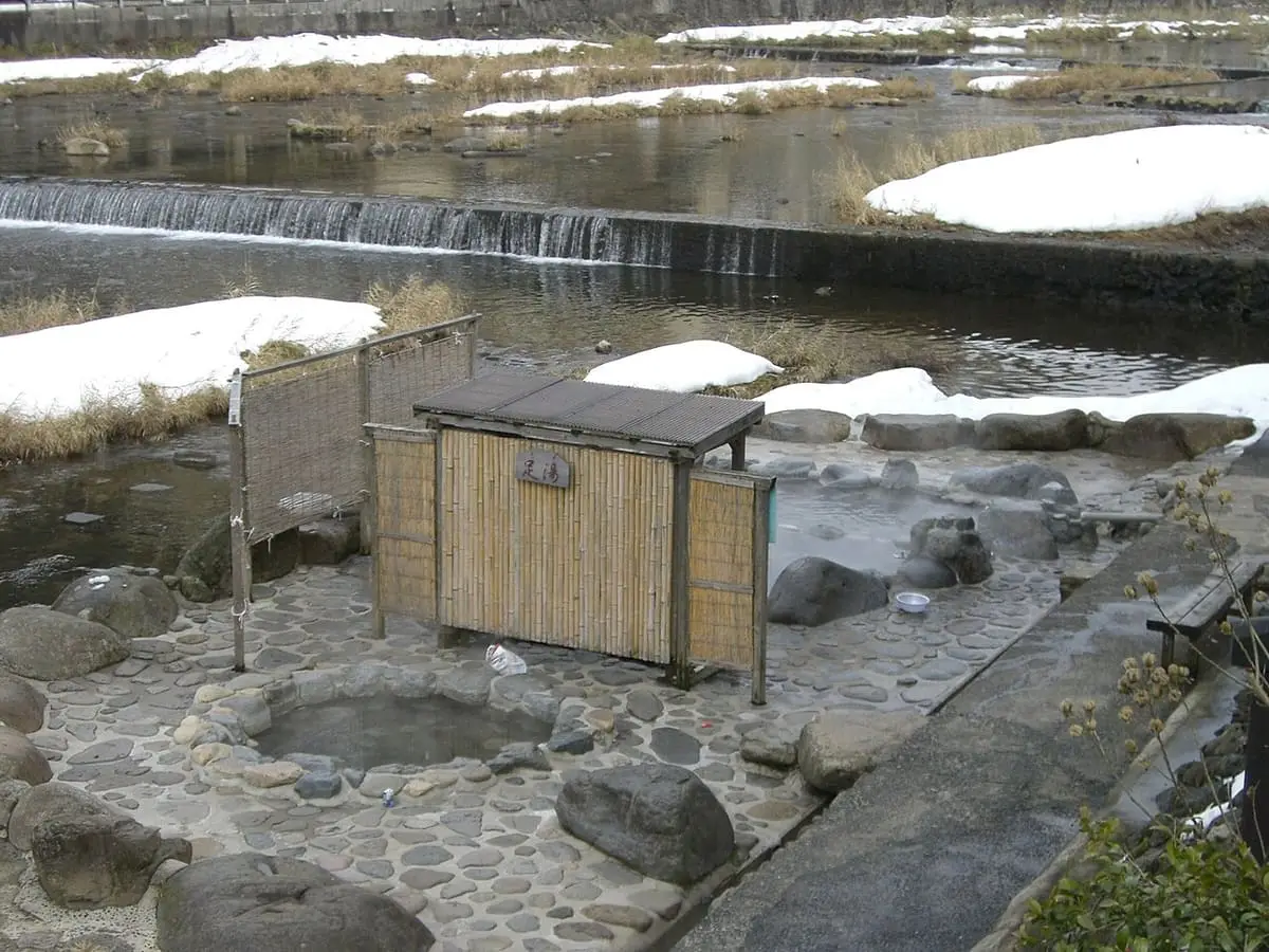 Stone riverbank bath and small wooden changing hut in snow at Misasa Onsen