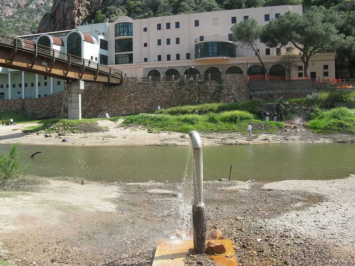 Hot spring water spouting from a pipe on the riverbank below the Casteldoria spa building