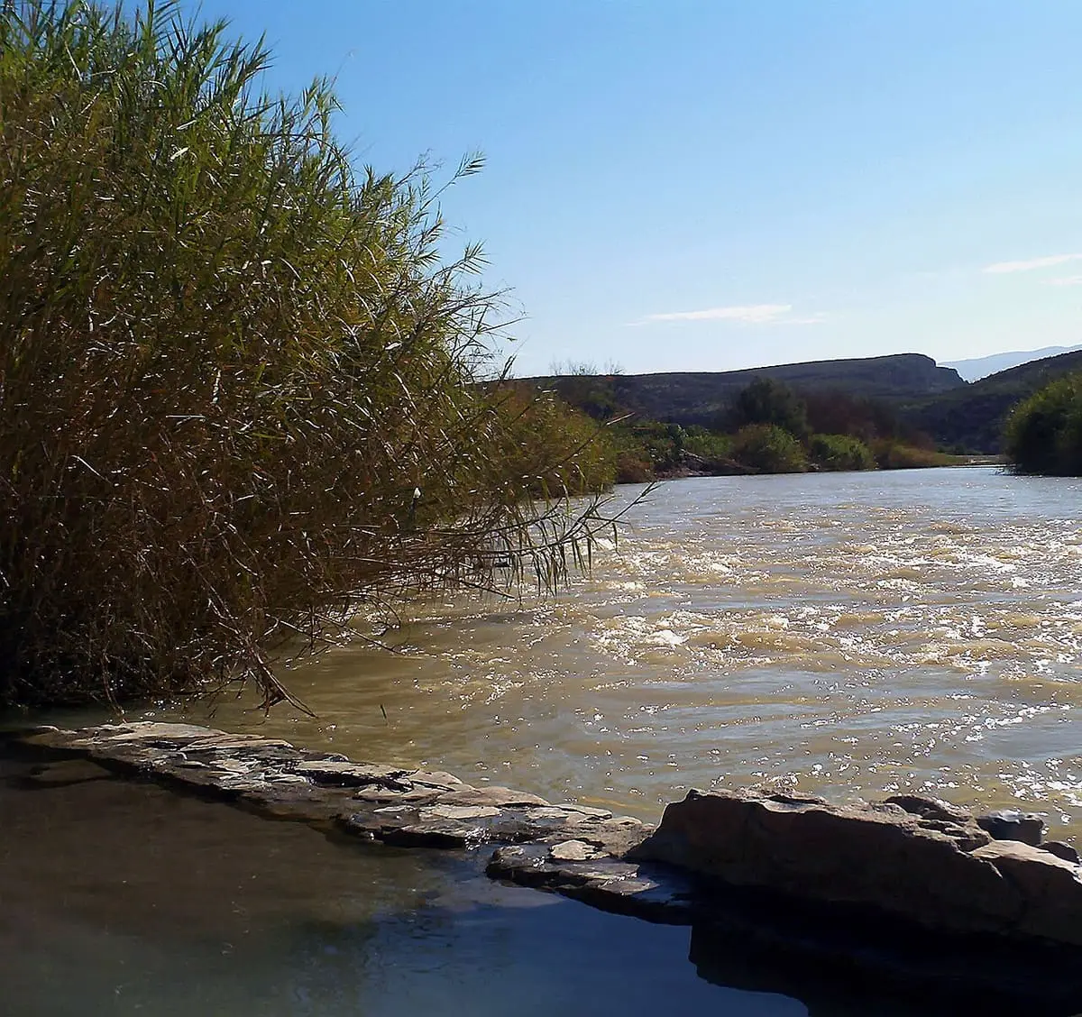 Rock wall of the hot spring pool beside the fast flowing Rio Grande and tall river cane