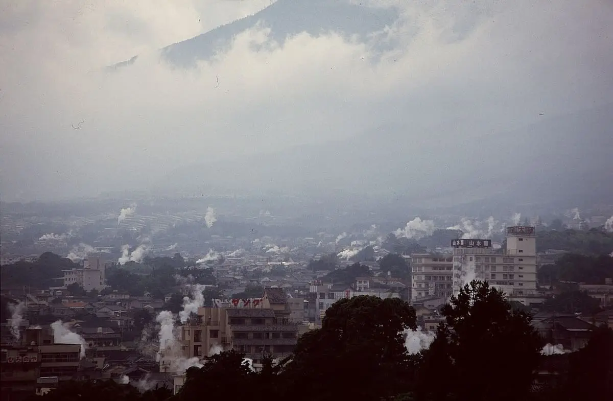 Steam rising from many hot spring vents across the city of Beppu below cloudy hills