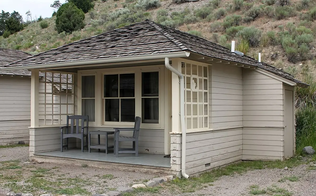 Small cream colored Mammoth Hot Springs Hotel cabin with porch and table on a sagebrush hillside