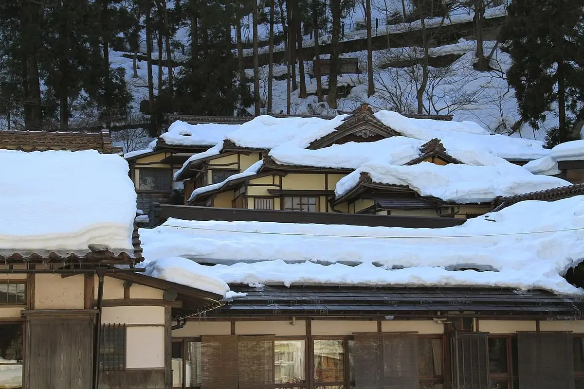 Snow covered roofs of old wooden inns at Higashiyama Onsen with wooded slopes behind