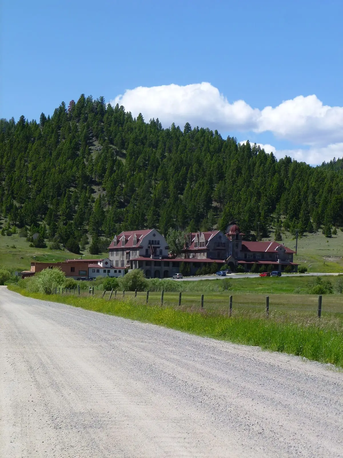 Gravel road leading to the Boulder Hot Springs Hotel below a forested hill
