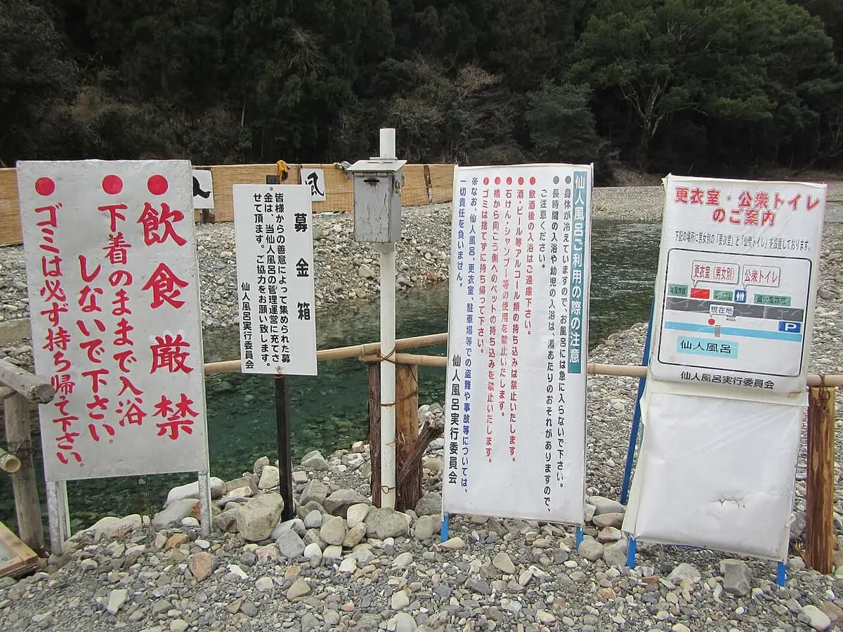 Sennin buro rule signs on the gravel bank beside the clear river bath at Kawayu Onsen