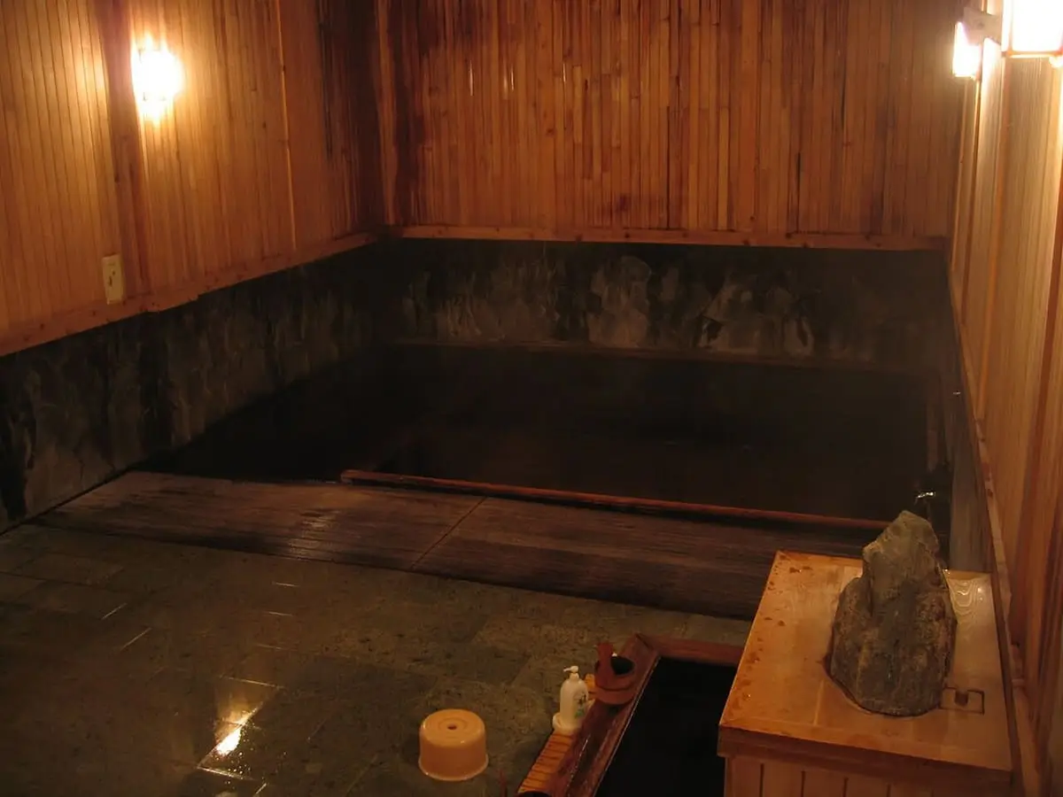 Wooden inner bath of Tsuta Onsen with dark water and warm lamplight