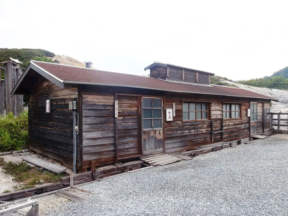 Weathered wooden Furutaki no Yu bath hut on gravel at Osorezan