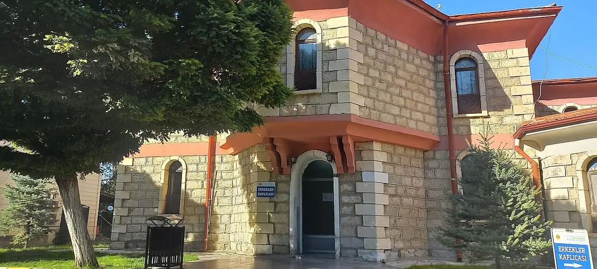 Arched windows and entrance of the stone Gazlıgöl thermal bath building beside a tree