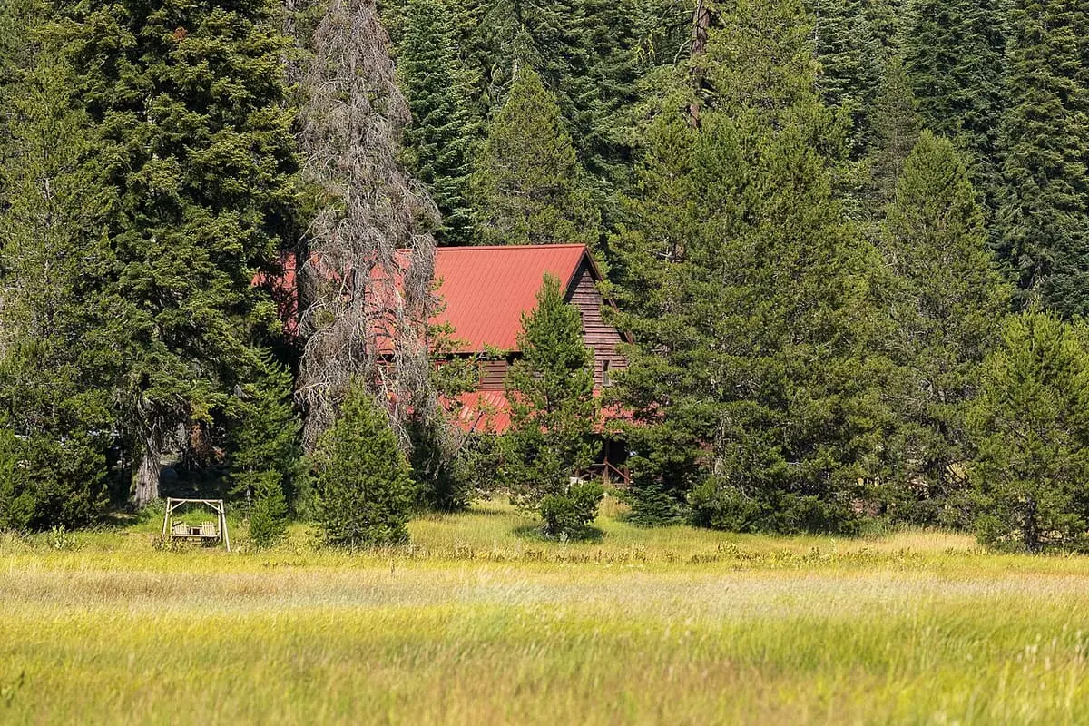 Red roofed Drakesbad Guest Ranch building among tall conifers above a green Warner Valley meadow