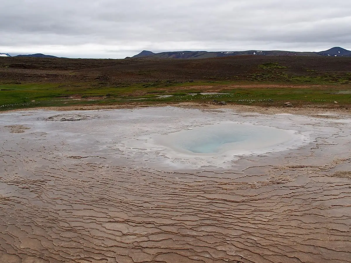Clear blue hot spring pool ringed by cracked sinter terraces at Hveravellir