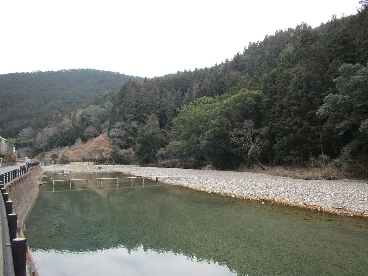 Clear green Oto River and wide gravel bar at Kawayu Onsen beneath forested slopes