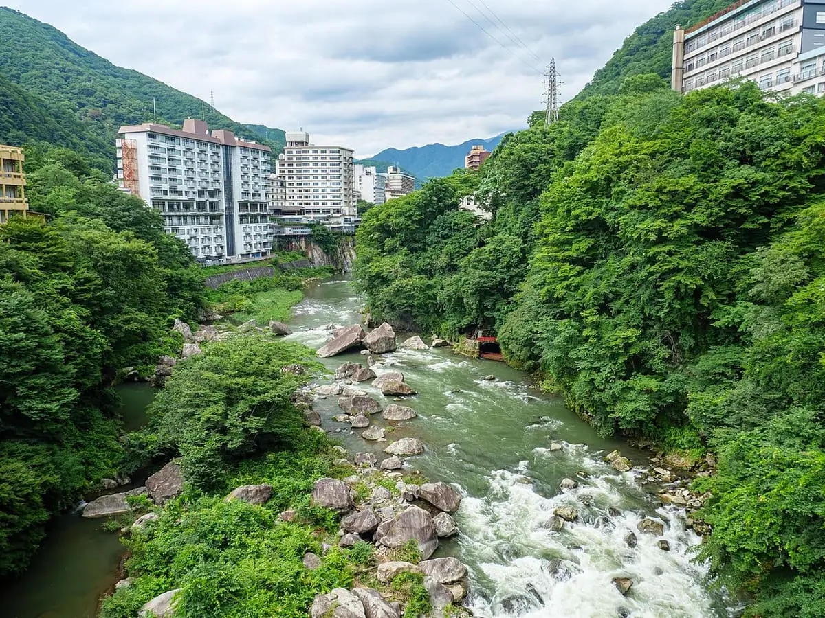 Rapids of the Kinugawa River between green banks with Kinugawa Onsen hotels upstream