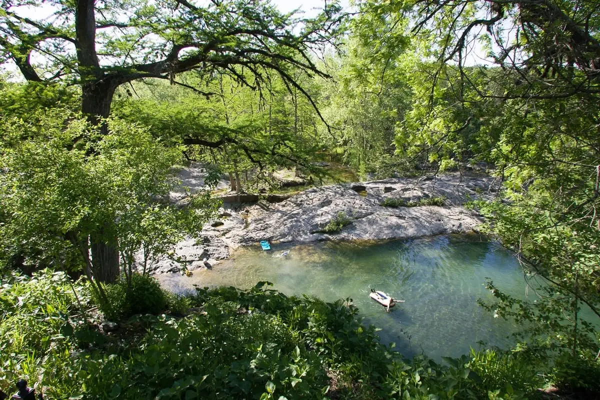 Overview of the main natural swimming area at Krause Springs below limestone ledges and trees