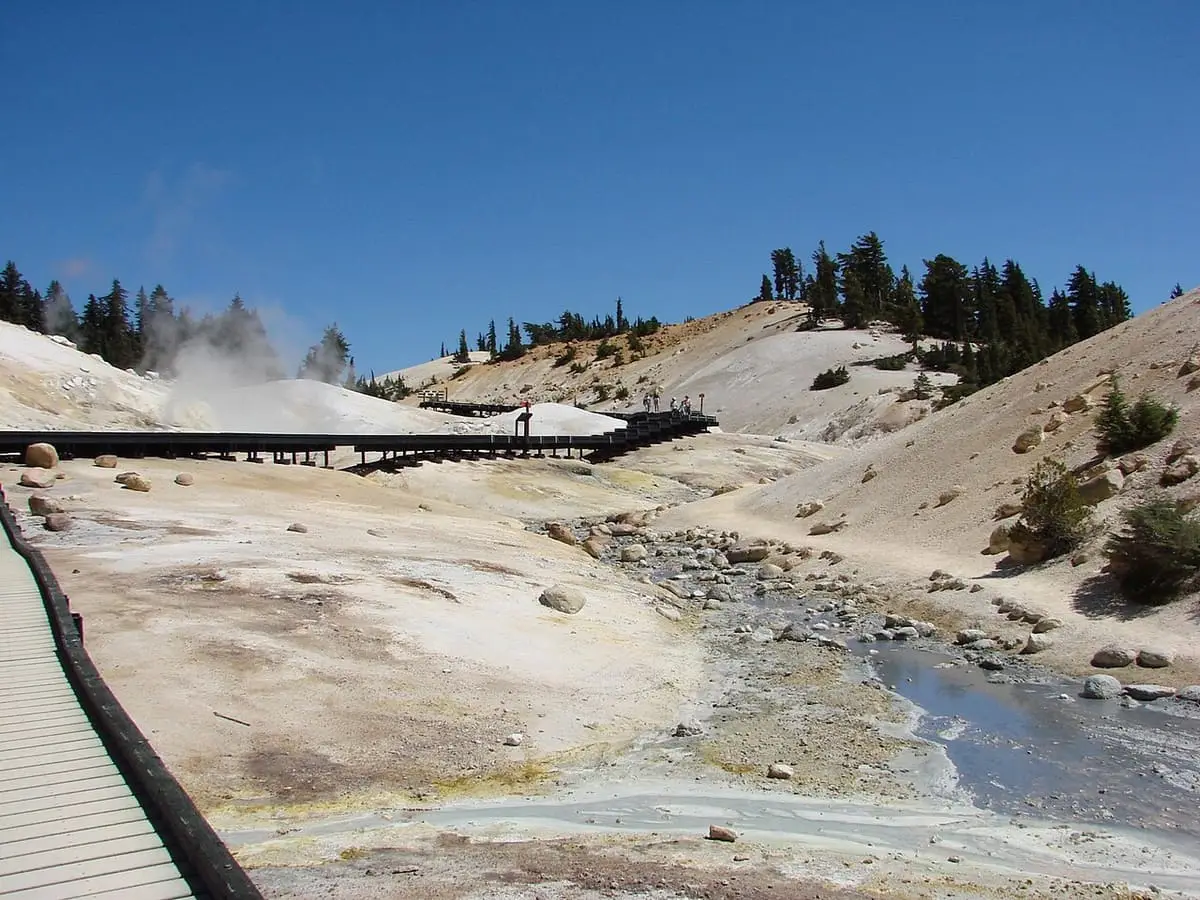Boardwalk crossing the barren Bumpass Hell hydrothermal basin with steam vents and a runoff stream