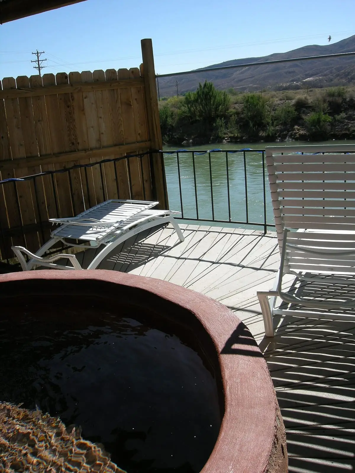 Round private soaking tub on a deck beside the Rio Grande with lounge chairs and desert hills