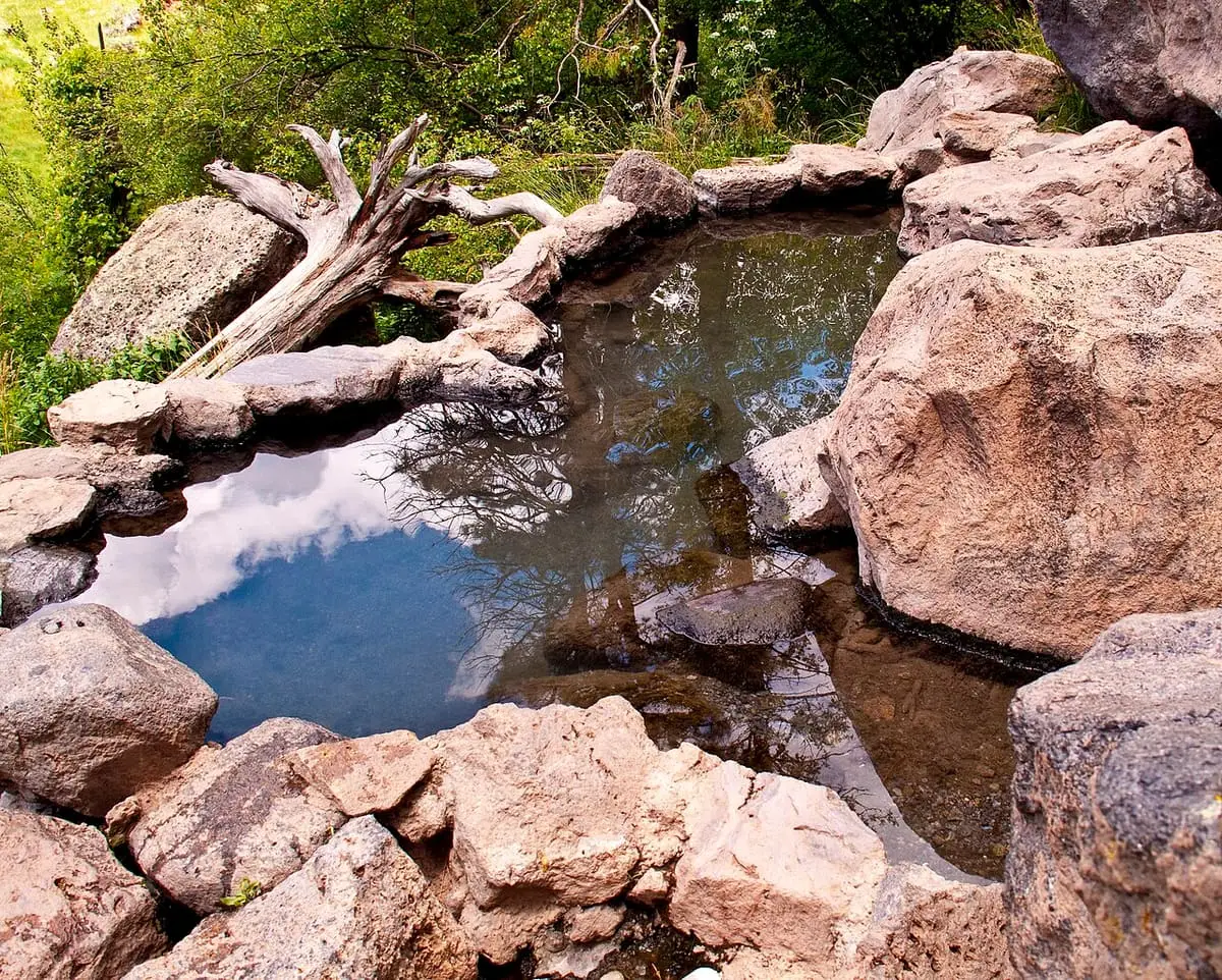 Boulder lined pool at Spence Hot Spring reflecting sky and trees