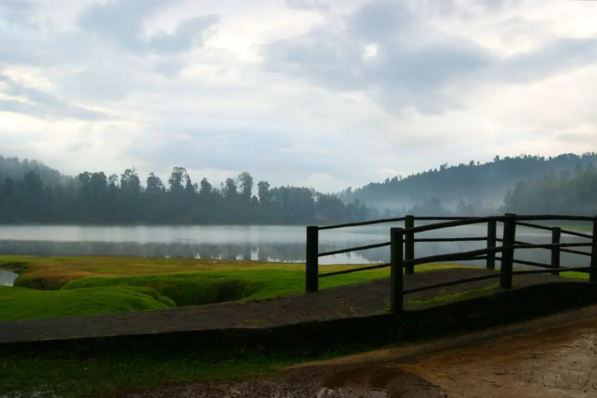 Wooden railing and footbridge beside Laguna Larga under a cloudy sky in Los Azufres