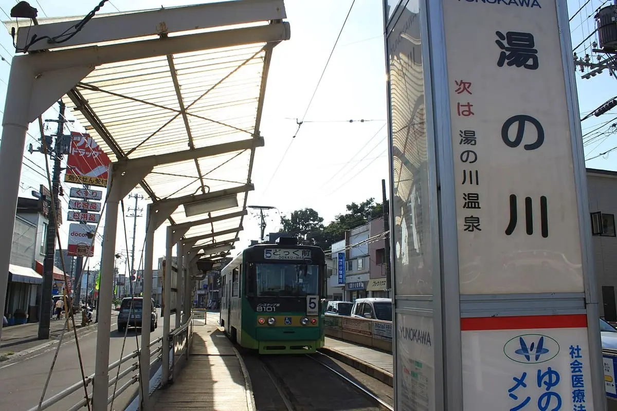 Yunokawa tram stop sign with a Hakodate streetcar at the platform