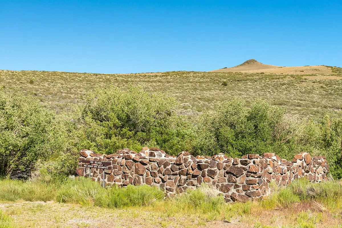 Low stone wall of the hot springs pool on Hart Mountain National Antelope Refuge below a distant butte