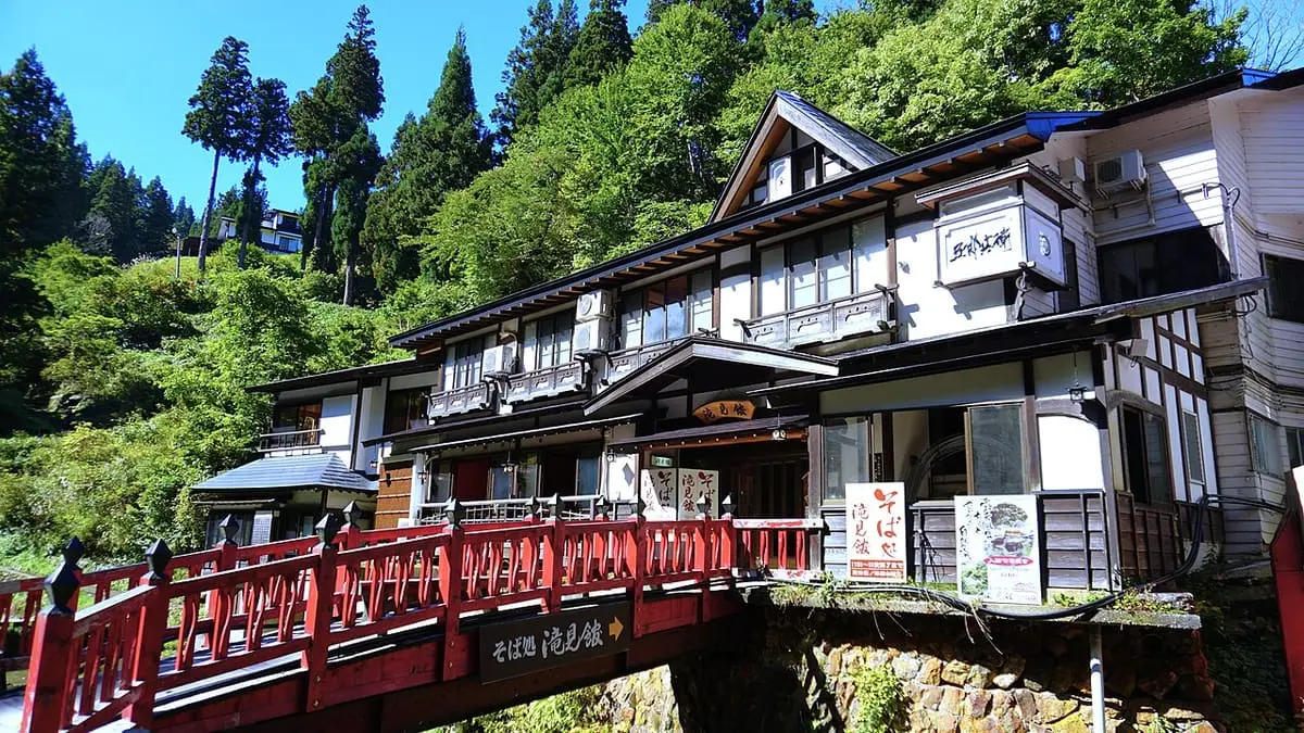 Red Takimi Bridge and the Takimi tei building surrounded by green forest in Ginzan Onsen
