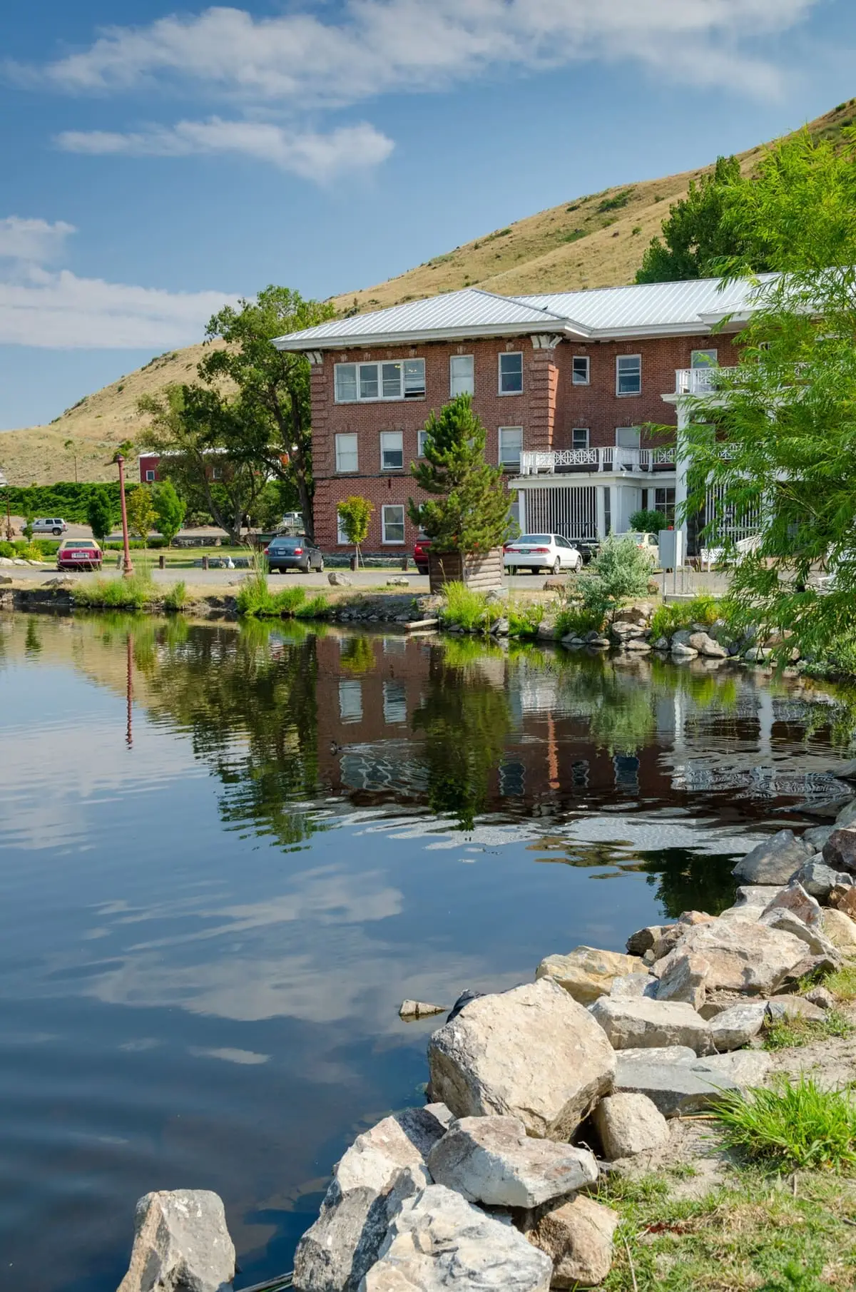 Hot Lake Springs Resort building reflected in the calm lake with rocks along the shore