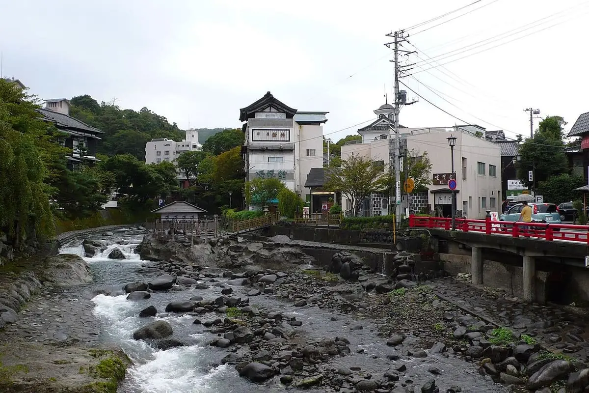 Rocky Shuzenji River with a red bridge and onsen town buildings under a cloudy sky