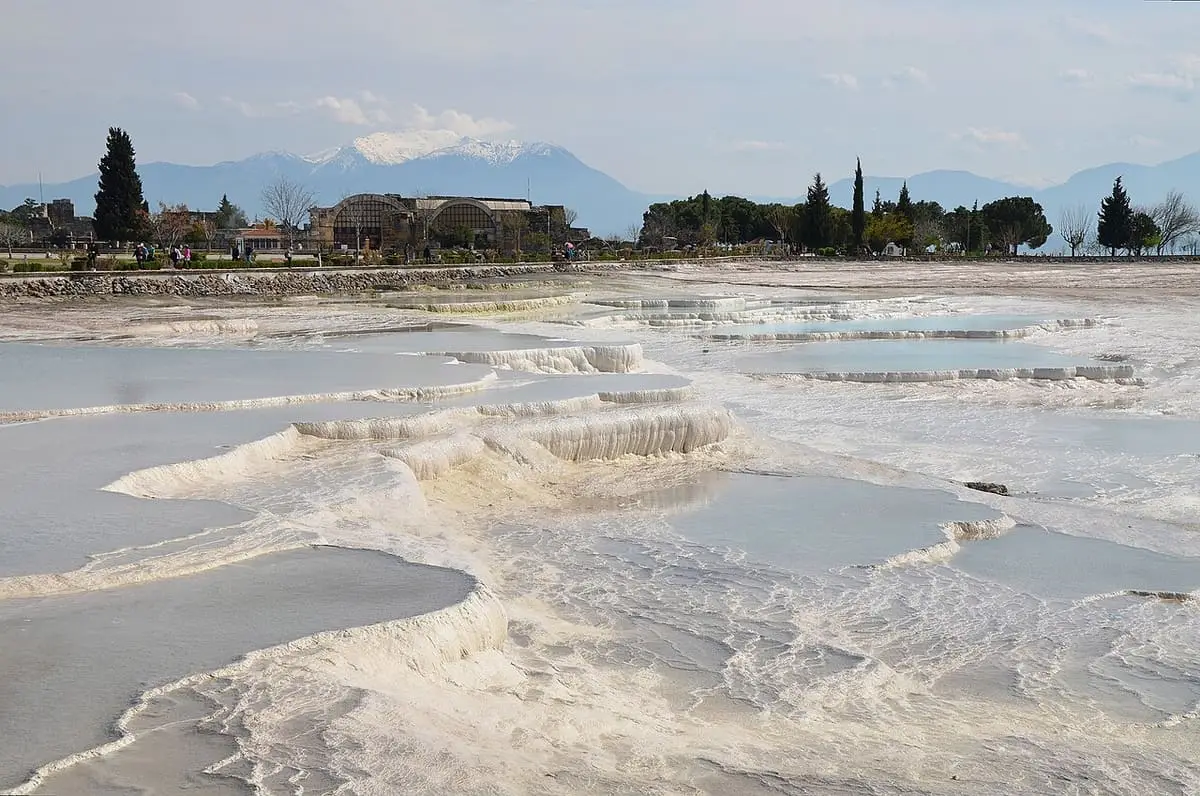 Wide view across the flooded travertine terraces of Pamukkale toward distant snowy mountains