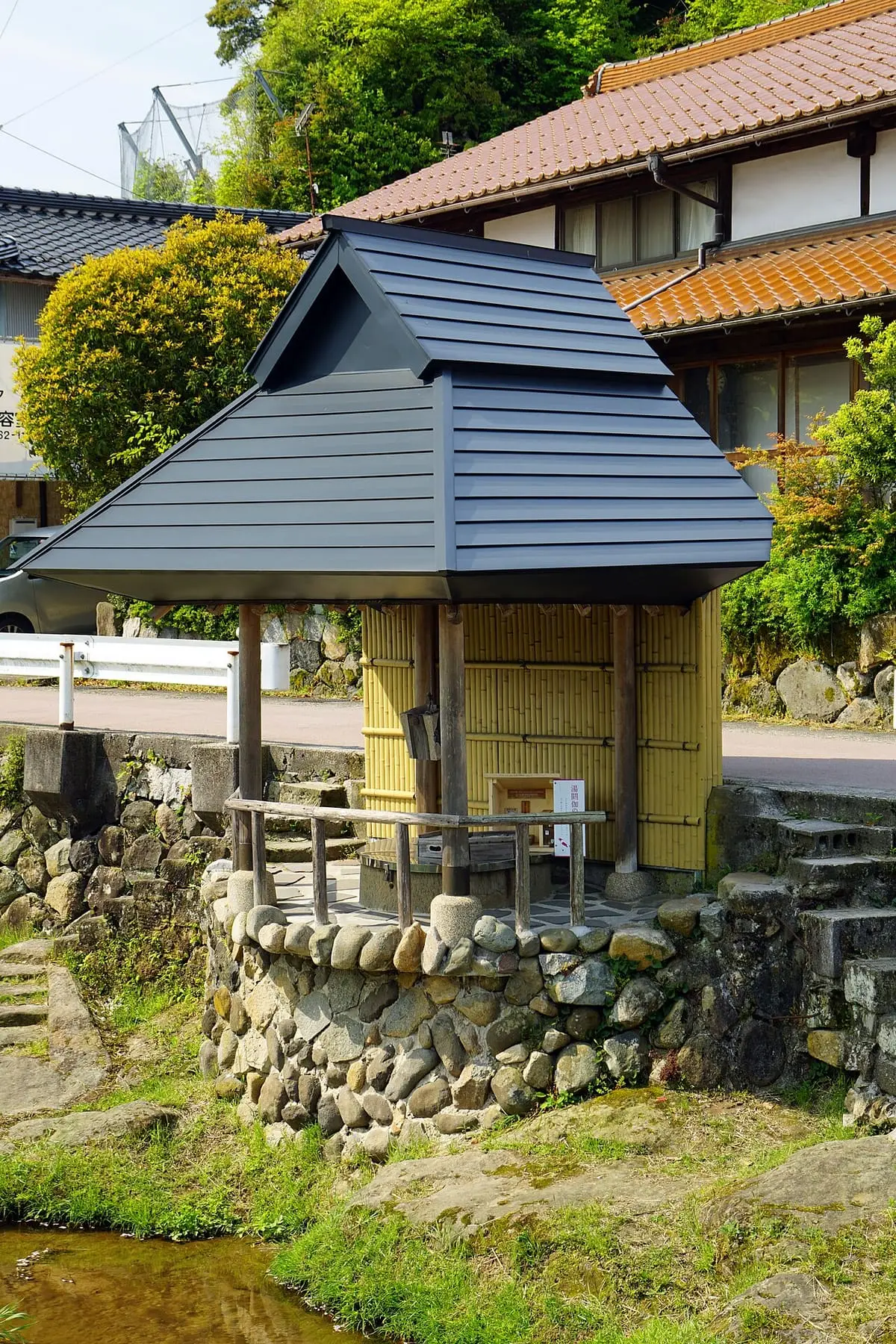 Small roofed wooden pavilion on a stone wall beside the stream in Tamatsukuri Onsen
