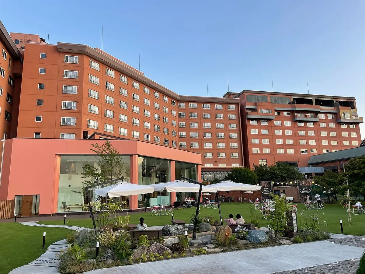 Large brick hotel of Toyako Onsen with a landscaped garden under blue sky