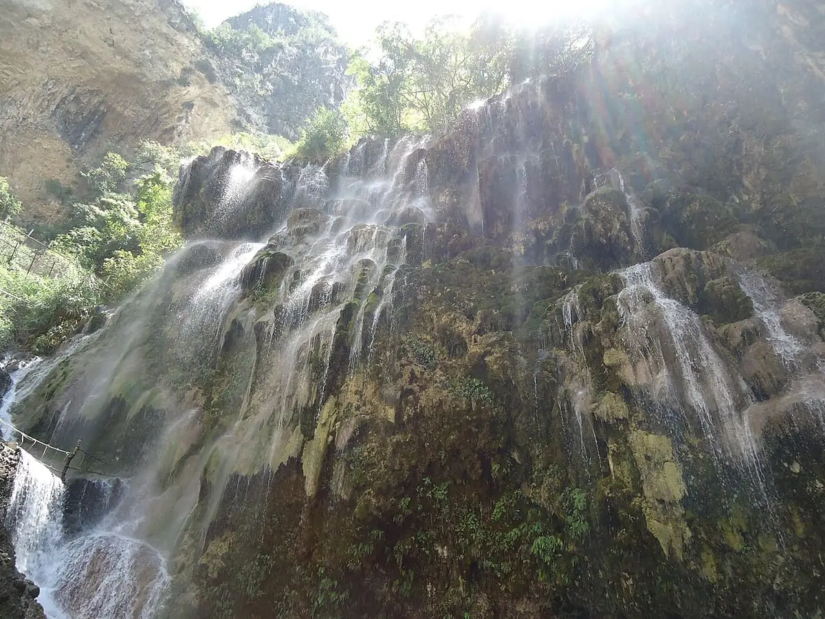 Sunlit waterfall spilling over a mineral cliff in the Tolantongo canyon