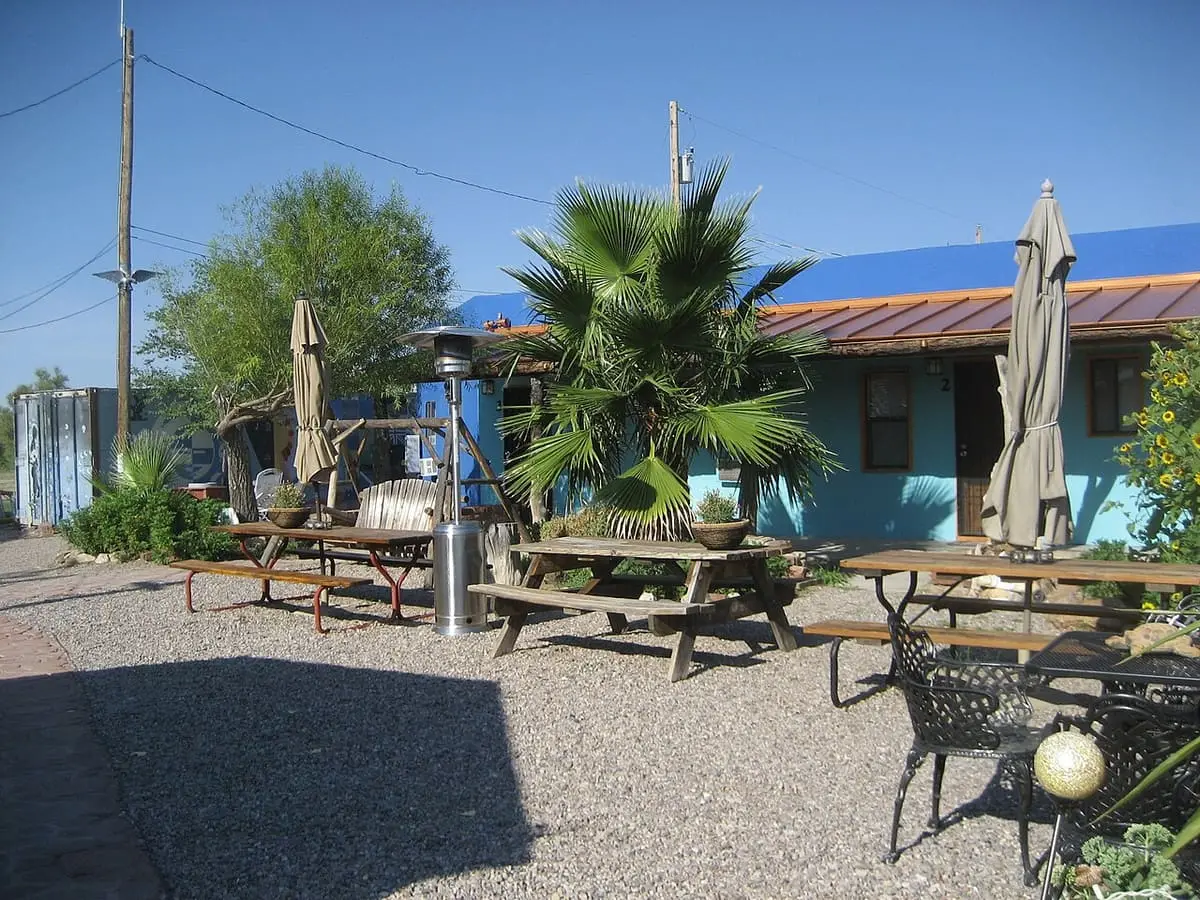 Gravel courtyard with picnic tables, umbrellas and a palm beside blue guest rooms at Riverbend