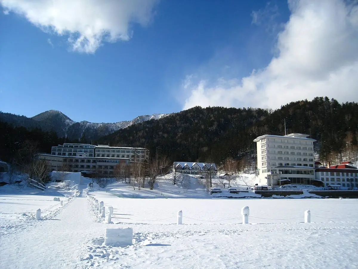 Lakeside hot spring hotels beside snow covered frozen Lake Shikaribetsu under blue sky