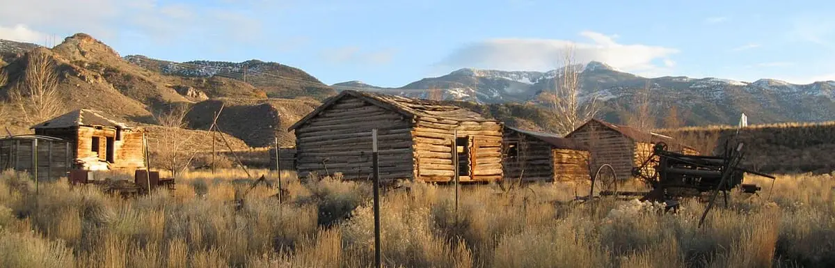 Row of old log cabins at Mystic Hot Springs below rugged hills and snowy peaks