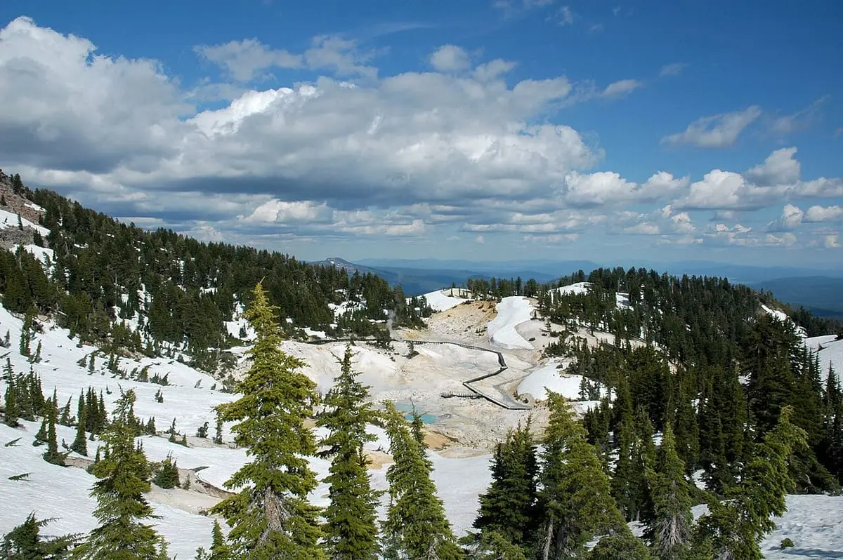 Bumpass Hell basin seen from the west among snow patches and conifers in Lassen Volcanic National Park